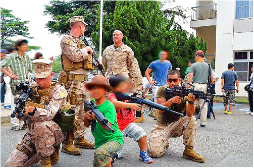 美国士兵让前来参观的儿童持枪并摆出射击的架势。